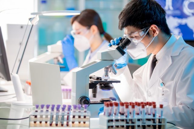 Investigador de biotecnología microbiólogo asiático usando microscopio en el laboratorio.