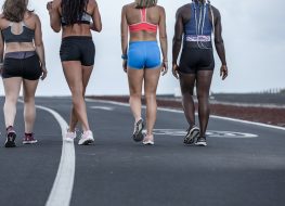 Back view of crop diverse female athletes in sportswear walking on asphalt road during outdoor workout in outskirts
