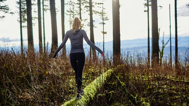 beautiful young girl walking in forest in running clothes standing on log
