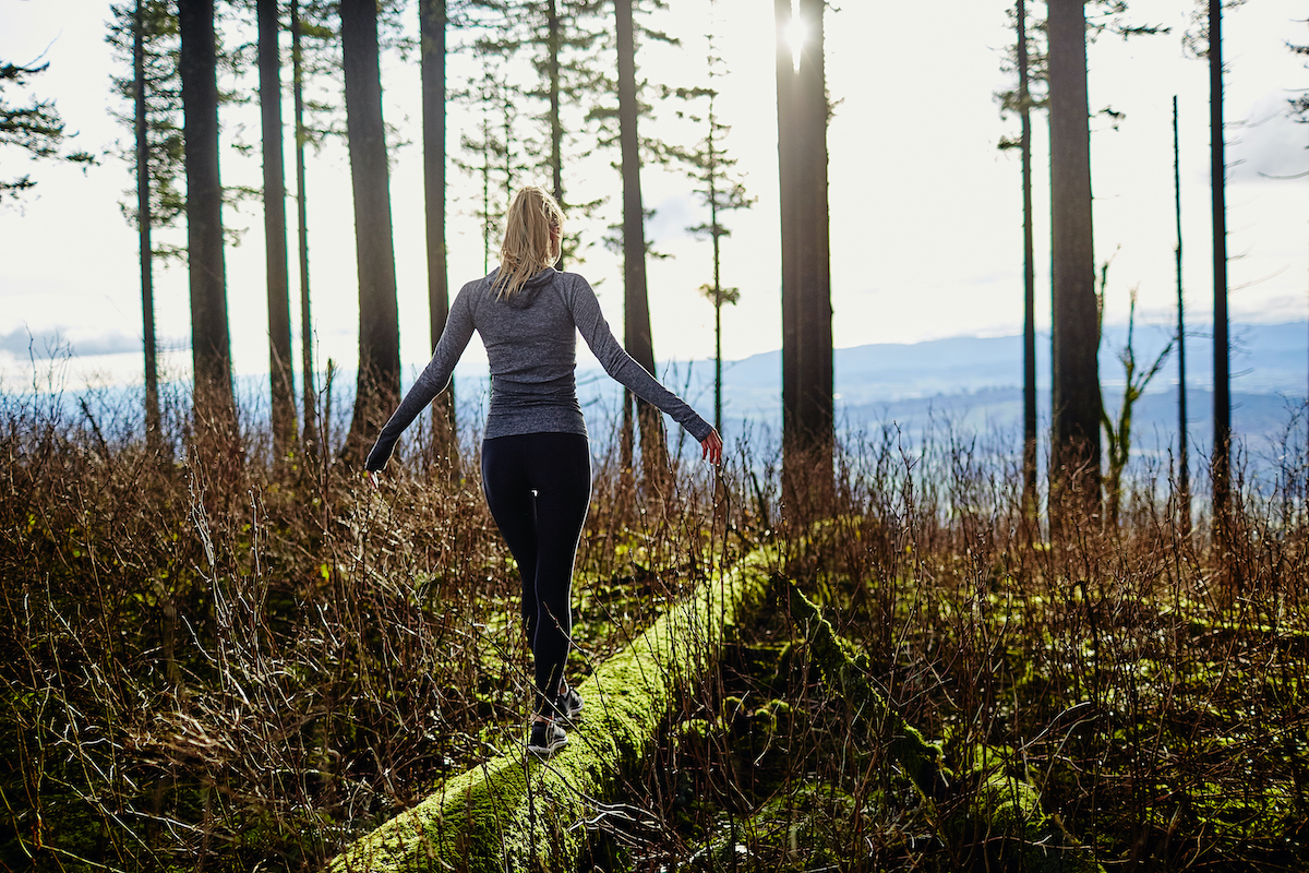 beautiful young girl walking in forest in running clothes standing on log