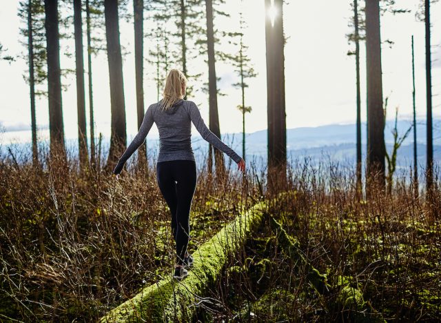 beautiful young girl walking in forest in running clothes standing on log
