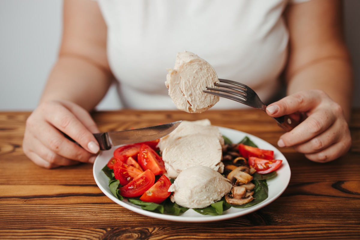 Woman eating baked chicken breasts with salad.