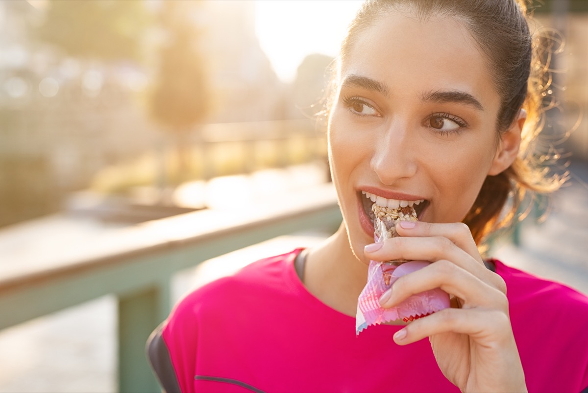 young woman eating protein bar during run