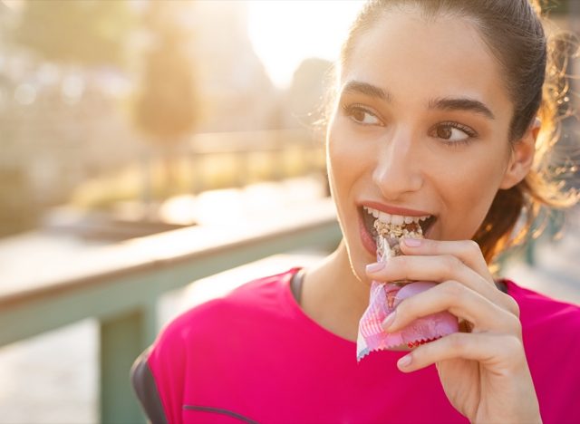 young woman eating protein bar during run