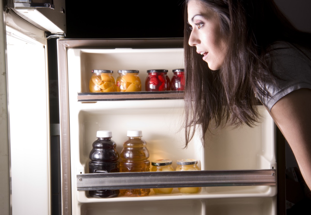 A woman raids the refrigerator late at night looking for a food snack.