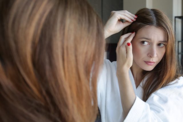 Woman examining her scalp and hair in front of the mirror.