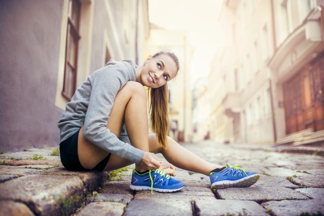 Young female runner is tying her running shoes on tiled pavement in old city center
