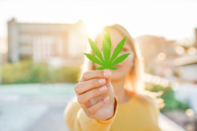 Young girl holding marijuana leaf with sunlight.