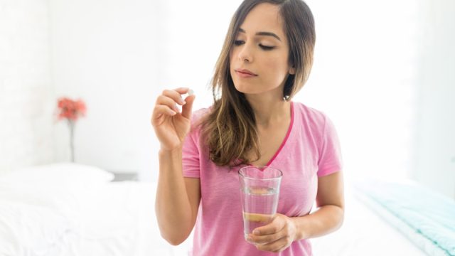 woman taking dose of medicine while sitting on bed