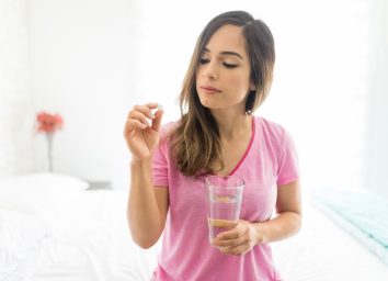 woman taking dose of medicine while sitting on bed