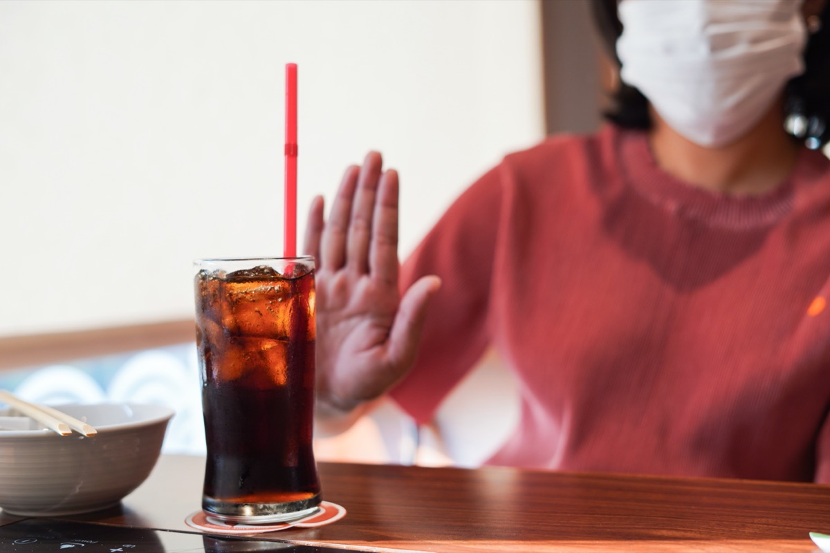 woman wearing mask refusing a glass of soda