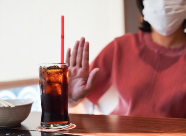 woman wearing mask refusing a glass of soda