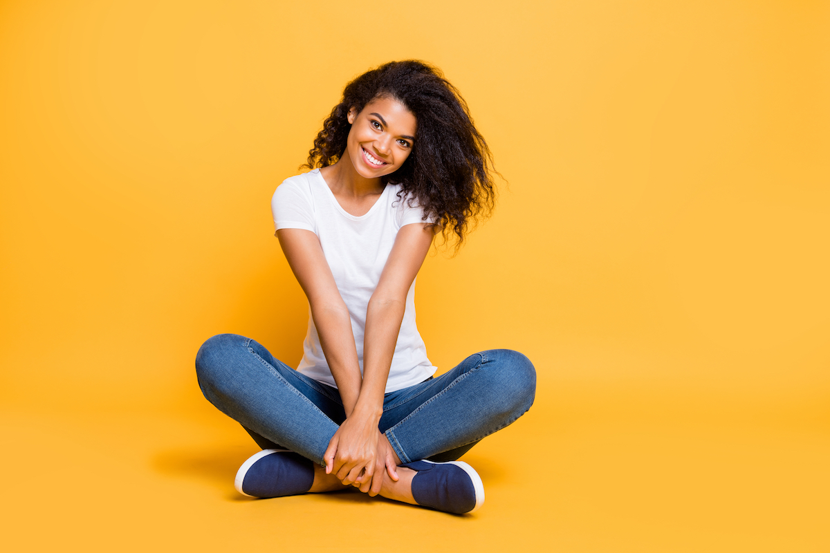 Full length body size photo of cheerful positive cute nice charming pretty girl in jeans denim footwear sitting with legs crossed isolated over vivid color background