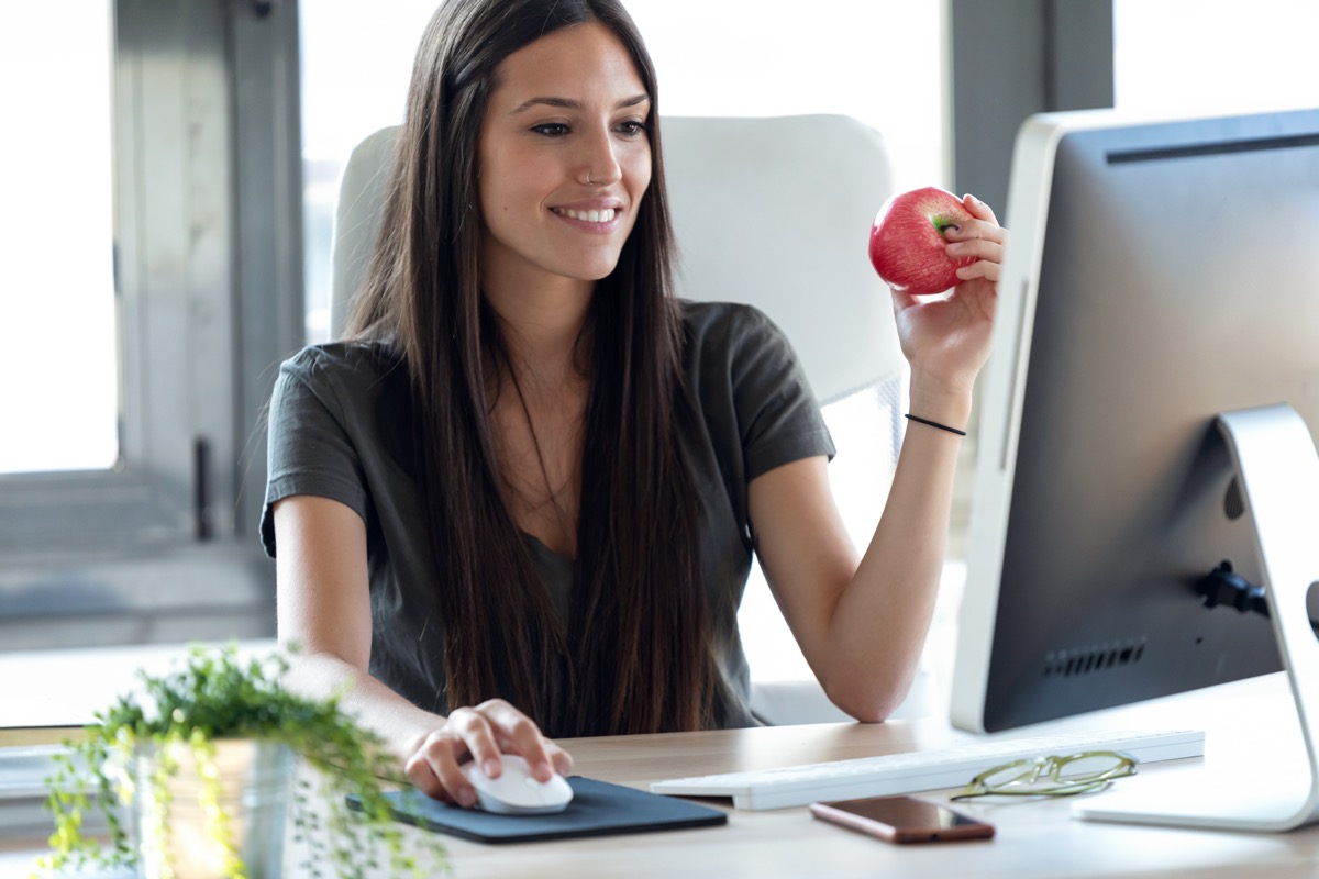 woman sitting at desk eating apple