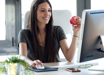 woman sitting at desk eating apple