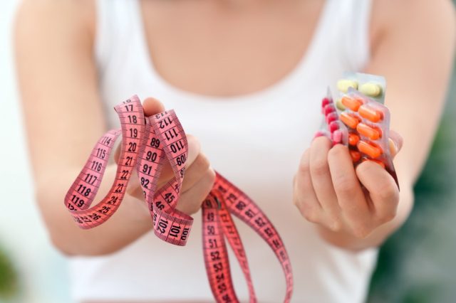 Woman holding packs of pills and measuring tape in hands.