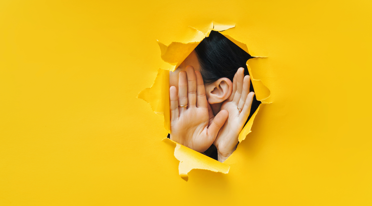 Female ear and hands close-up. Copy space. Torn paper, yellow background. The concept of eavesdropping, espionage, gossip and the yellow press.