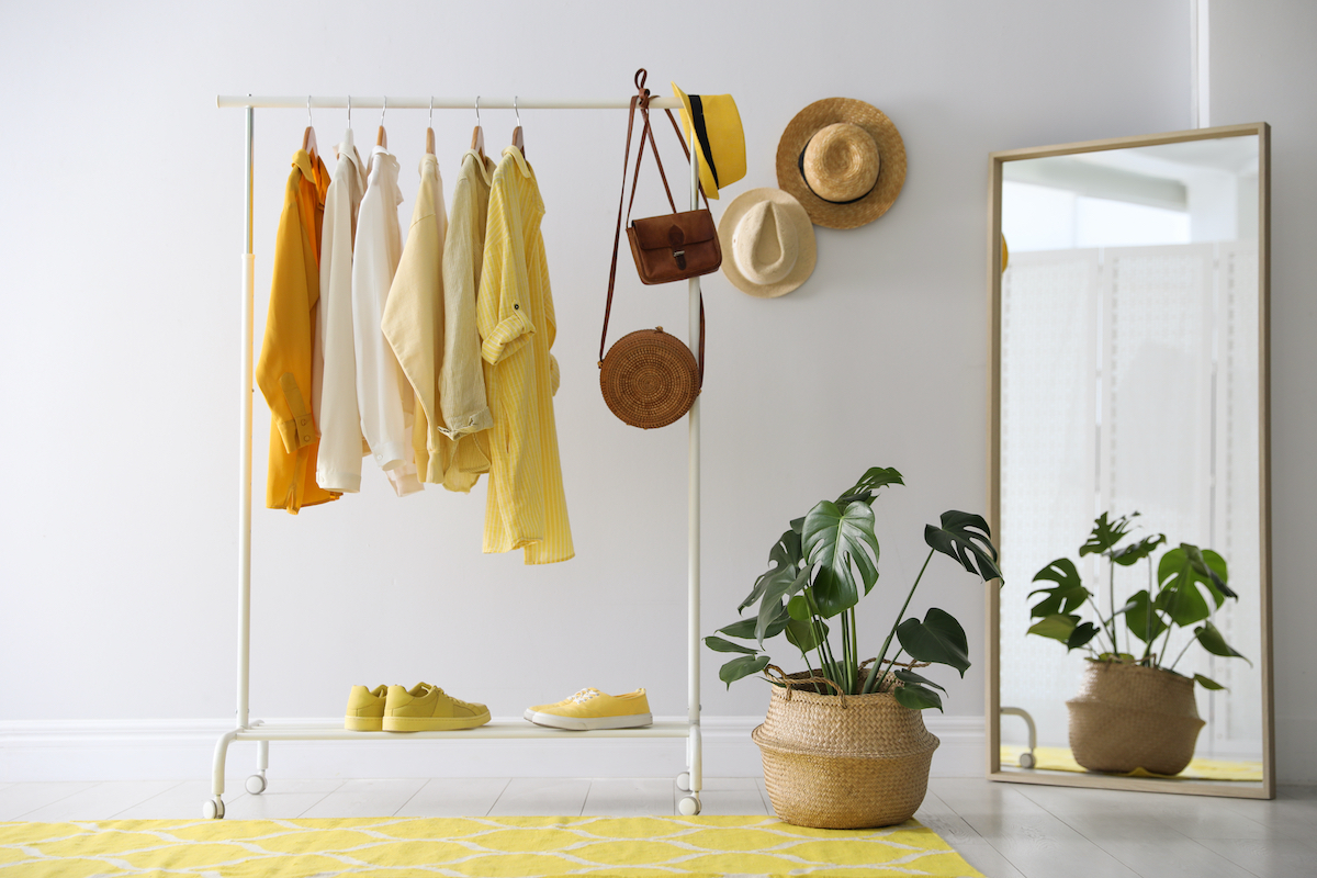Rack with stylish women's clothes and mirror indoors. Interior design yellow