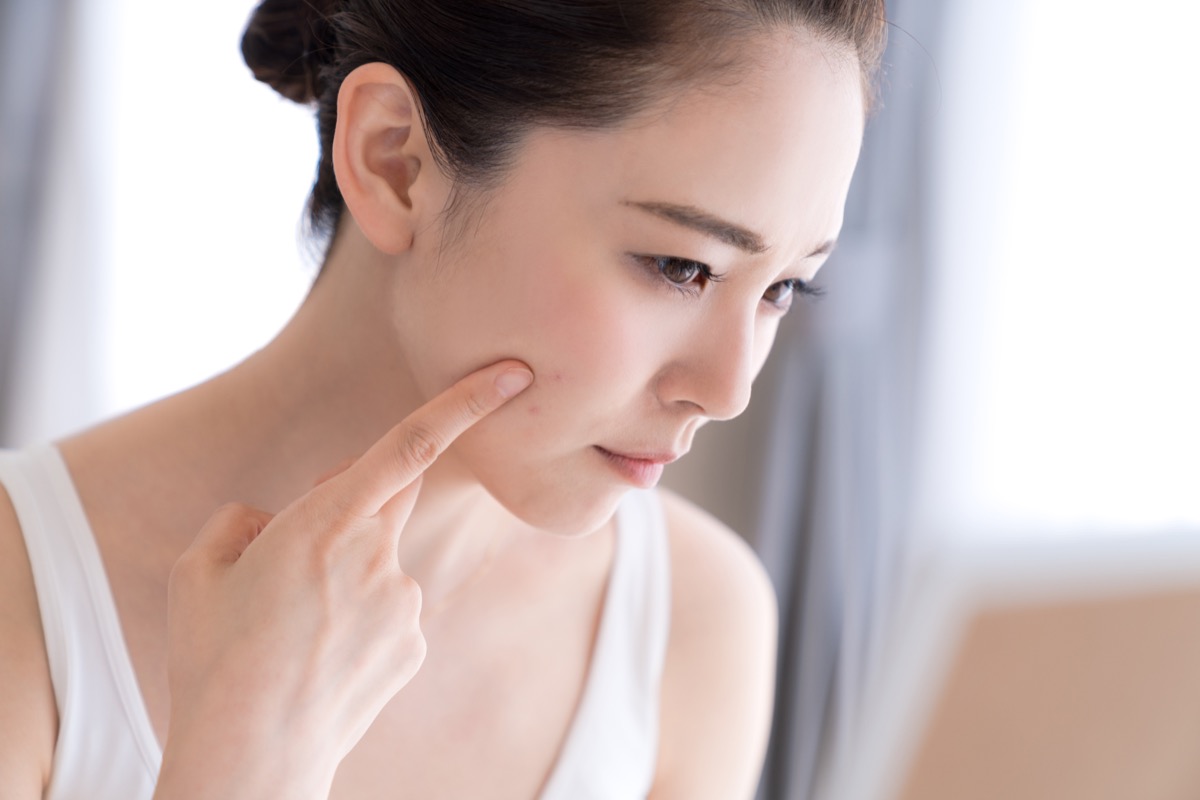 young woman looking in mirror touching face