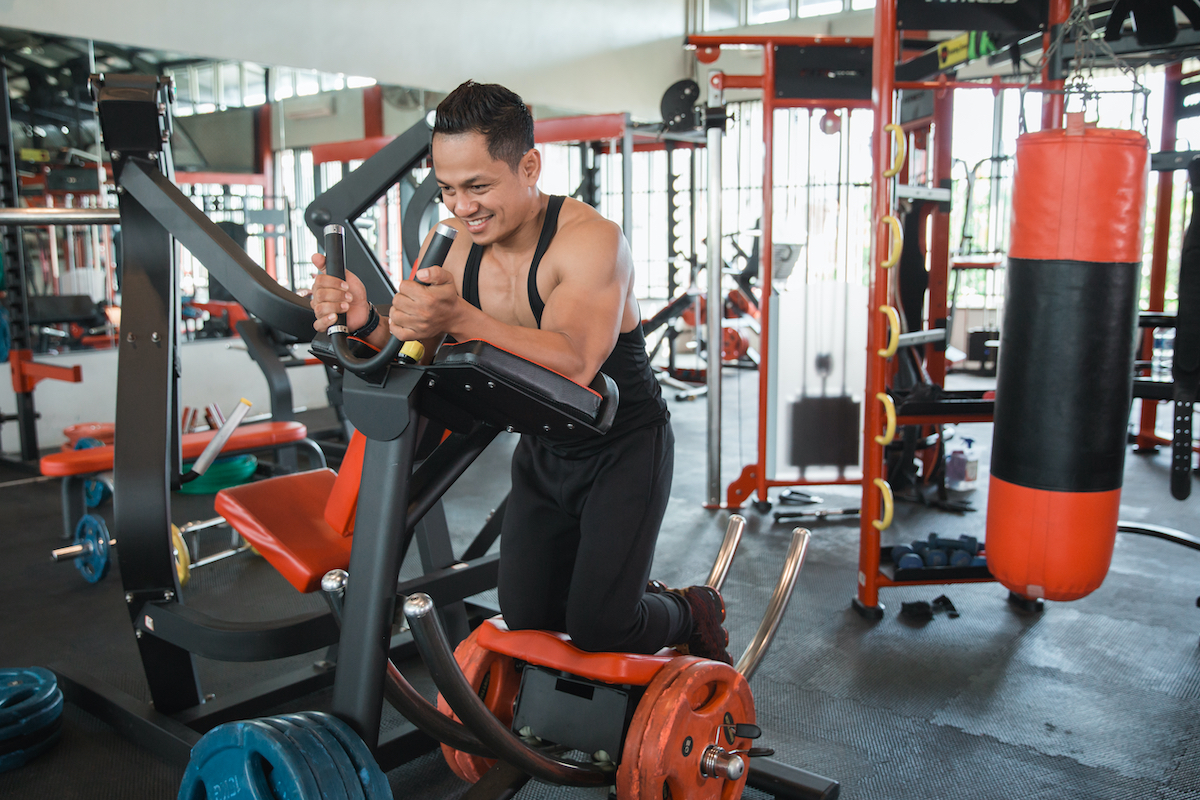 Athletic muscular man doing abs exercise on abdominal coaster gym machine