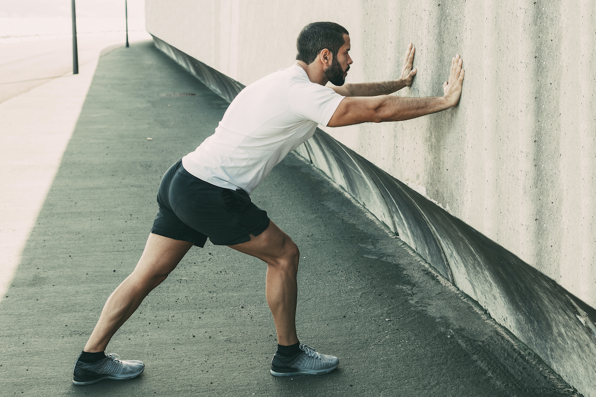 Strong Man Stretching Calf and Leaning on Wall