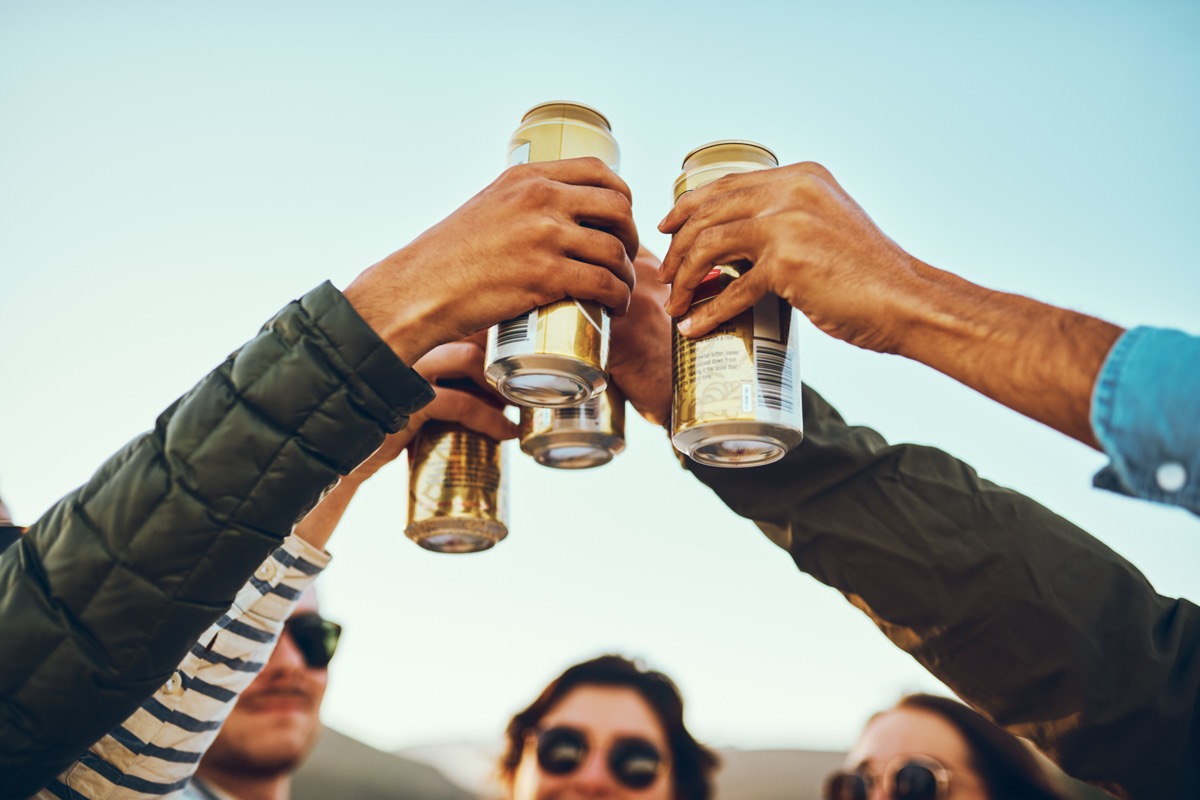 A group of young friends cheersing with beers while enjoying their day out on the beach.