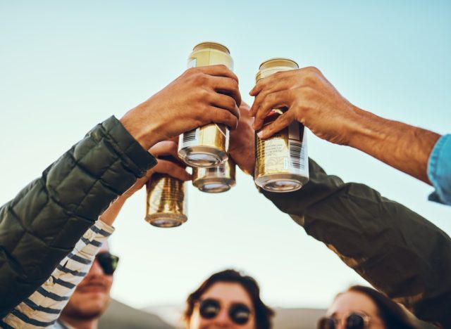 A group of young friends cheersing with beers while enjoying their day out on the beach.