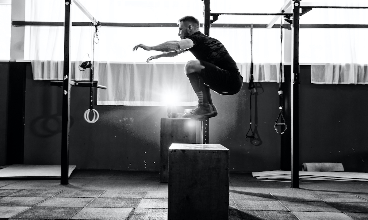 Fit young man jumping onto a box as part of exercise routine. Man doing box jump in the gym. Athlete is performing box jumps