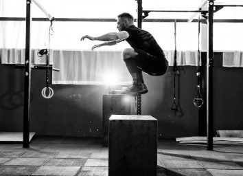 Fit young man jumping onto a box as part of exercise routine. Man doing box jump in the gym. Athlete is performing box jumps