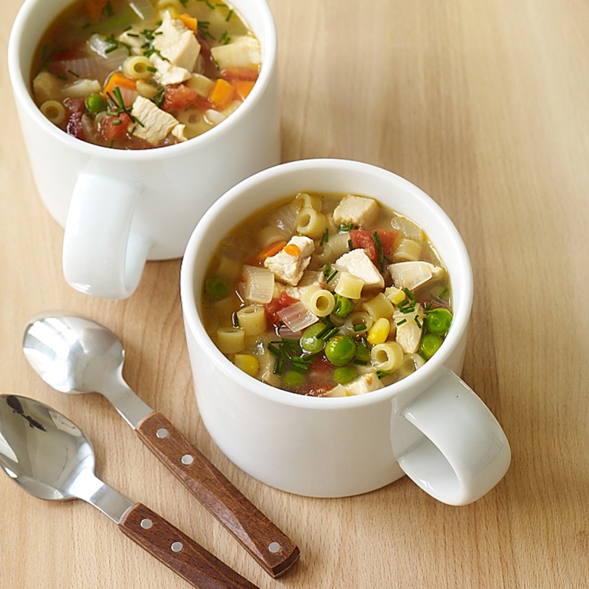 chicken noodle soup in two white mugs