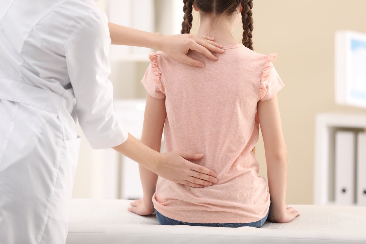 Chiropractor examining child with back pain in clinic.