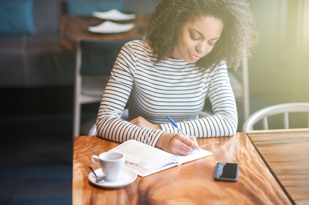 young woman drinking coffee and writing in journal