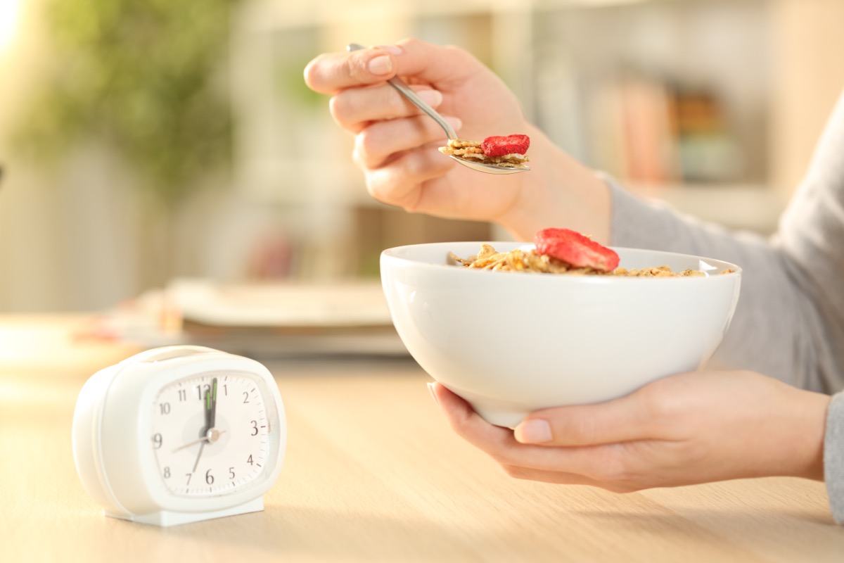 woman eating cereal in front of clock