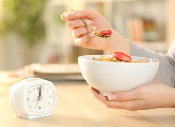 woman eating cereal in front of clock