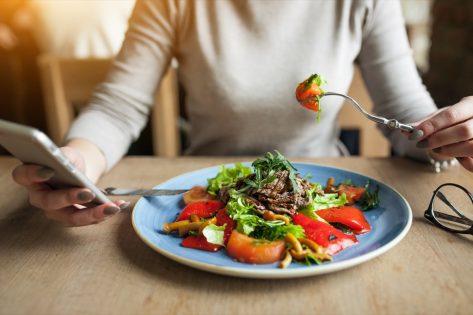 woman eating salad and tracking calories on cell phone
