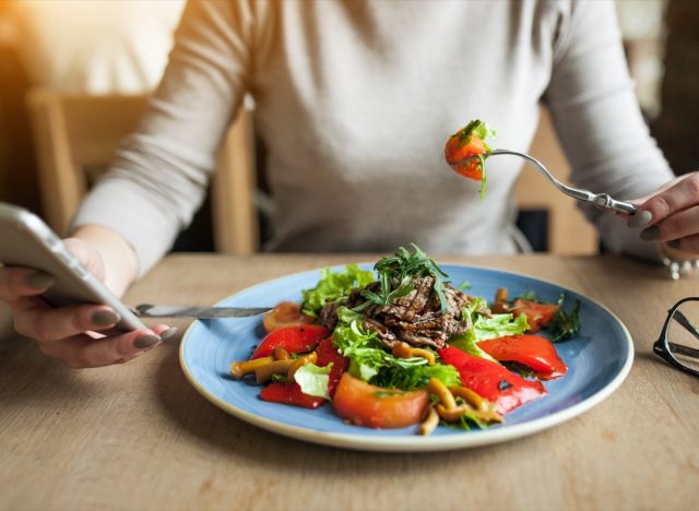 woman eating salad and tracking calories on cell phone