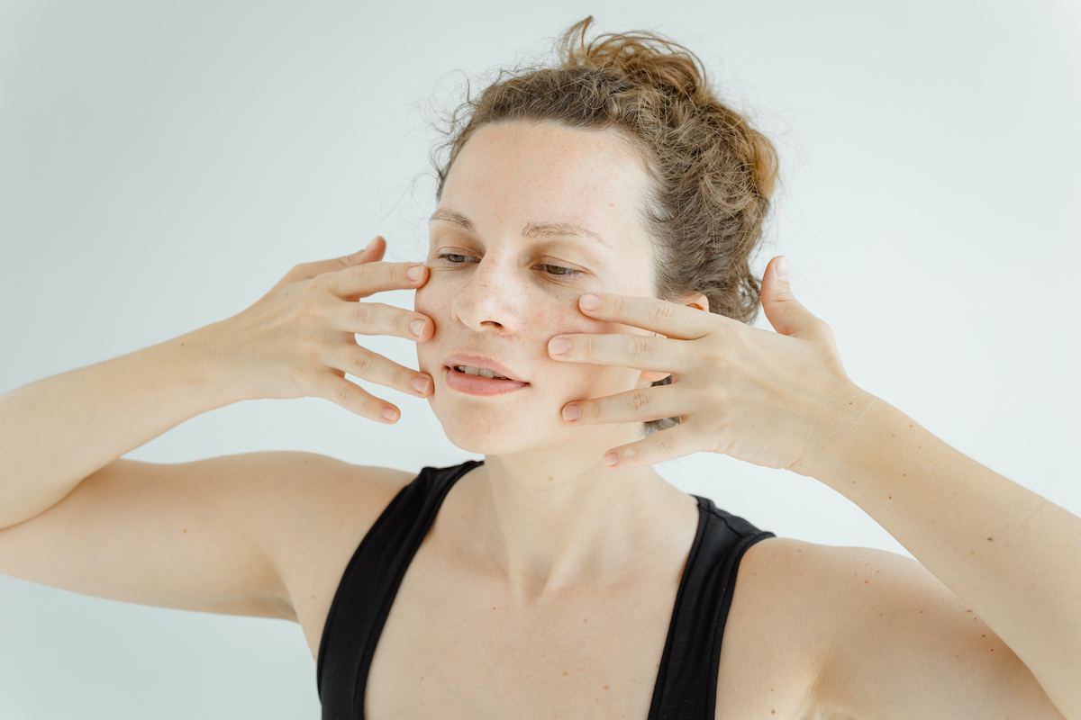 Gymnastics for the face. Cute white woman in black sleeveless sports shirt performing facial yoga. The concept of non-surgical rejuvenation and self-care.