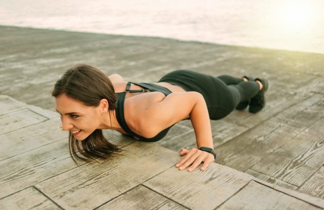 Young woman in tracksuit doing push-ups on the beach