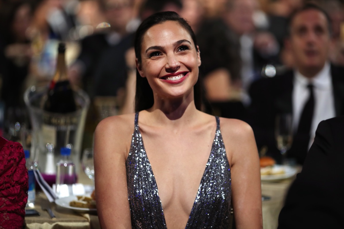 gal gadot in plunging sparkly silver dress smiling while seated