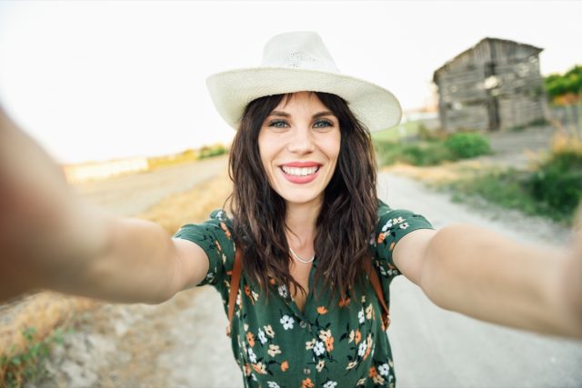 Hiker young woman, wearing flowered shirt, taking a selfie photograph outdoors