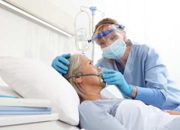 A nurse puts oxygen mask on elderly woman patient lying in the hospital room bed.