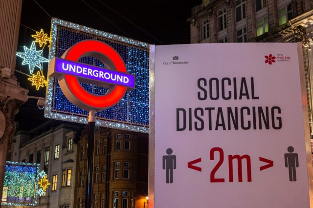 A social distancing sign, pictured next to the London Underground sign at Oxford Circus Station in London, UK.