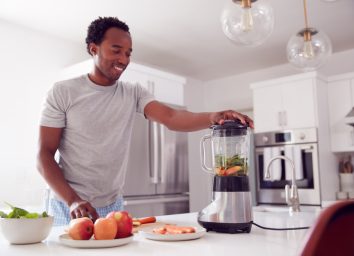 young man making smoothie in modern kitchen