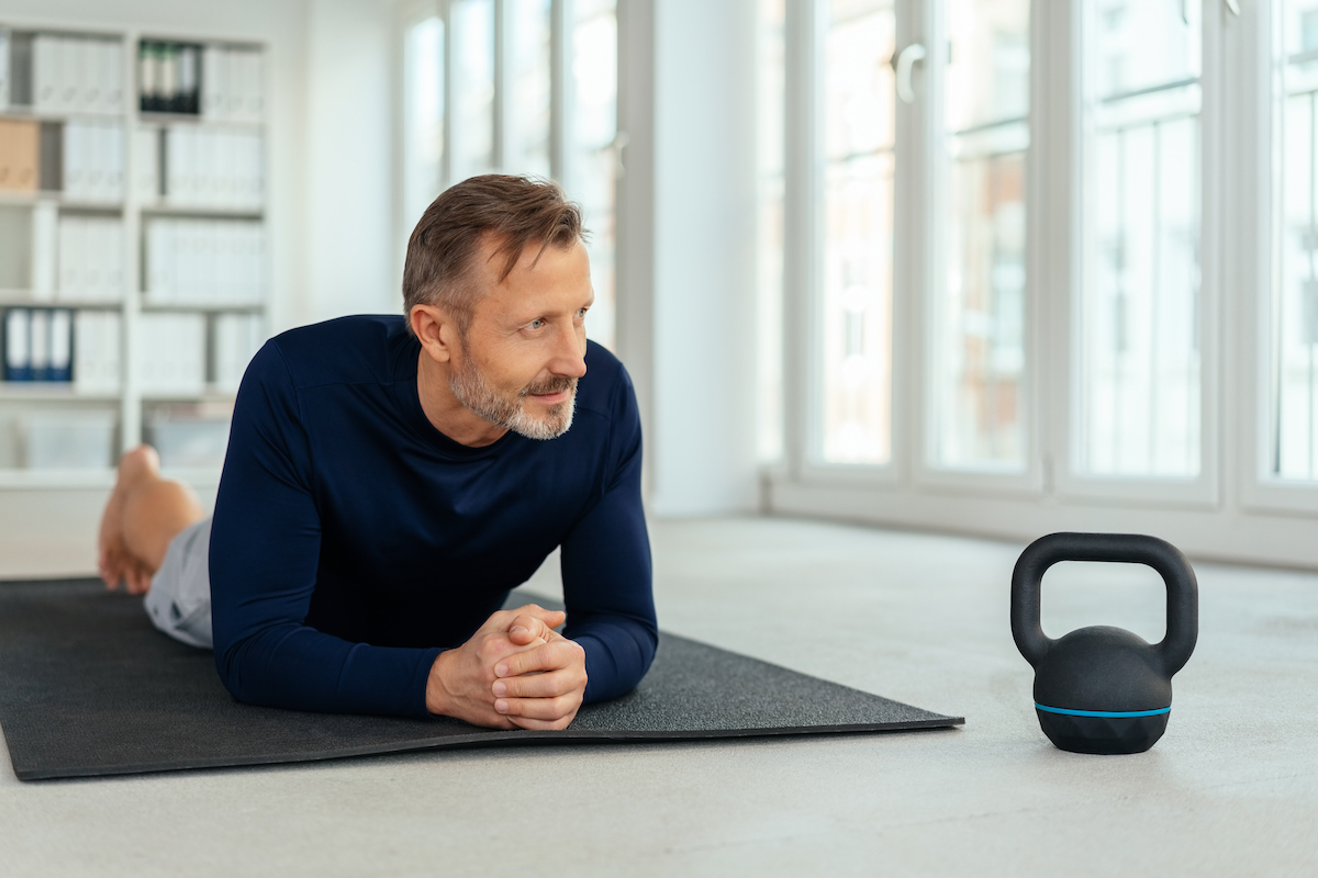 Man resting on a gym mat alongside a kettle weight as he takes a break from working out in a health and fitness concept