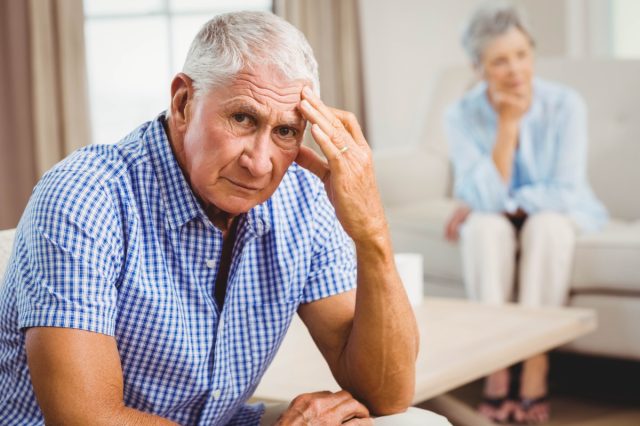 Portrait of worried senior man sitting on sofa in living room