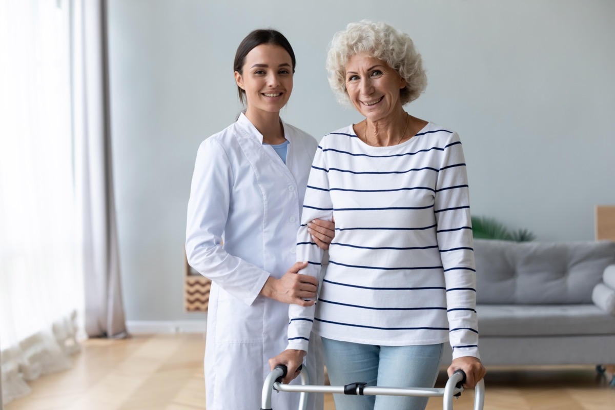 Female carer physiotherapist help happy old woman patient stand with walker.