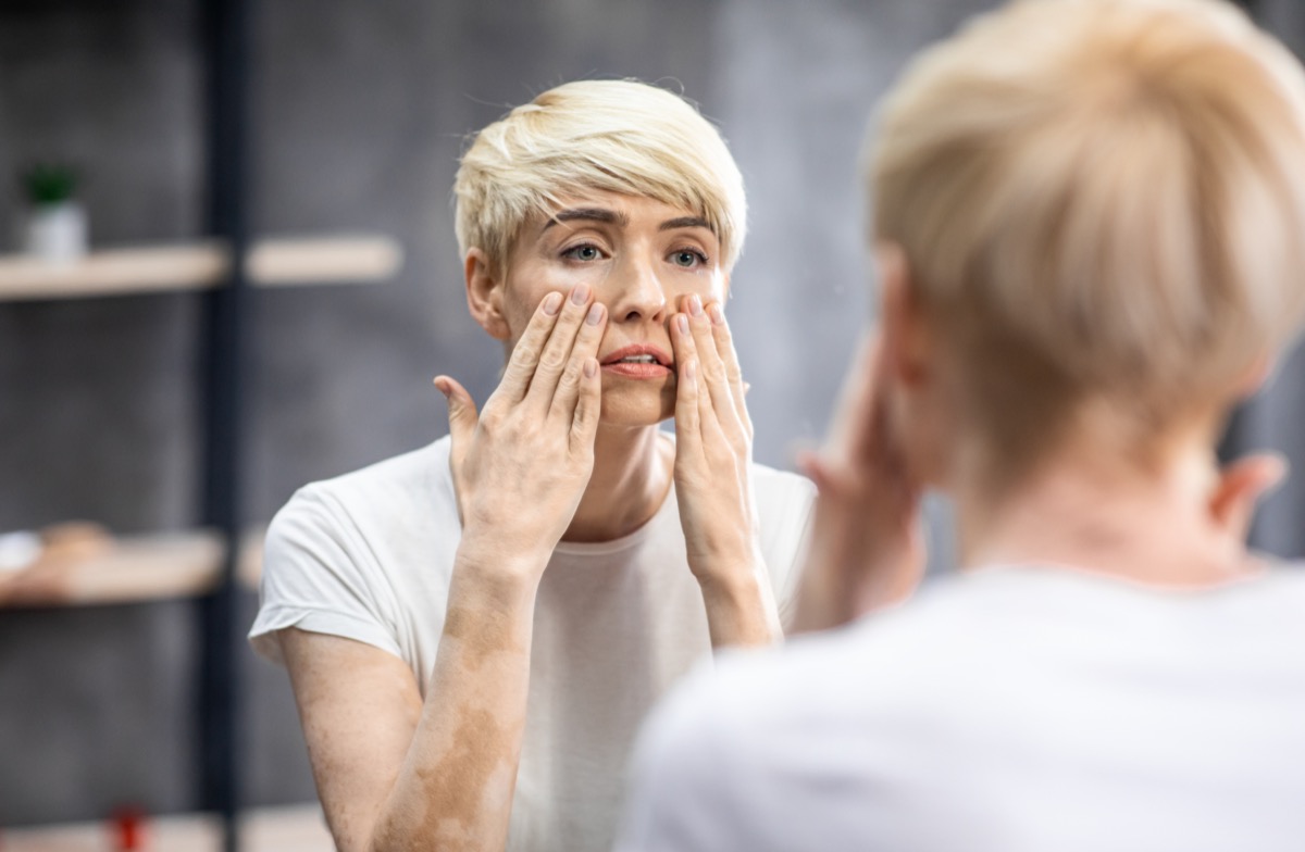 Woman touching face looking at mirror standing in bathroom