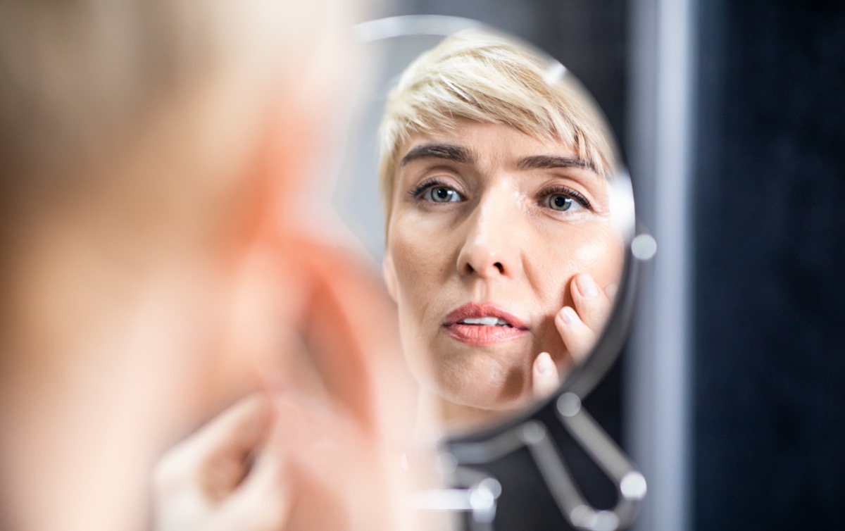 Mature woman looking in the mirror touching face standing in bathroom.
