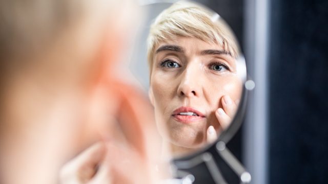 Mature woman looking in the mirror touching face standing in bathroom.