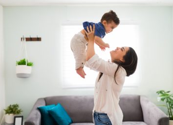 Happy young woman holding up her baby boy up while standing in living room